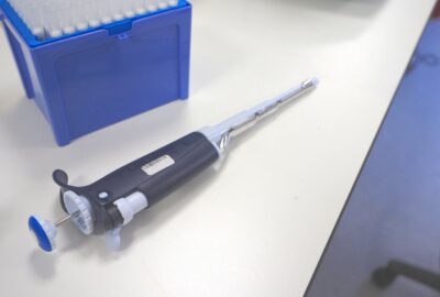 Open blue pipette tip box in upper left corner of image with dark blue and white pipette without tip lying on a white lab table